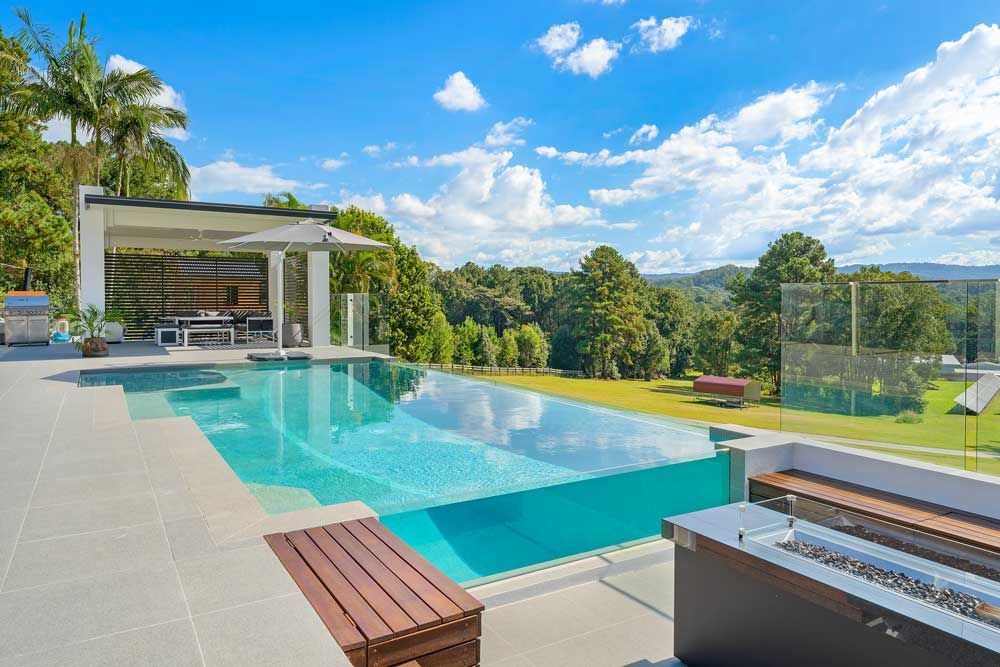 There is a Large Swimming Pool With a Clear Glass Bottom Surrounded by Trees — Pools By Design in Warana, QLD