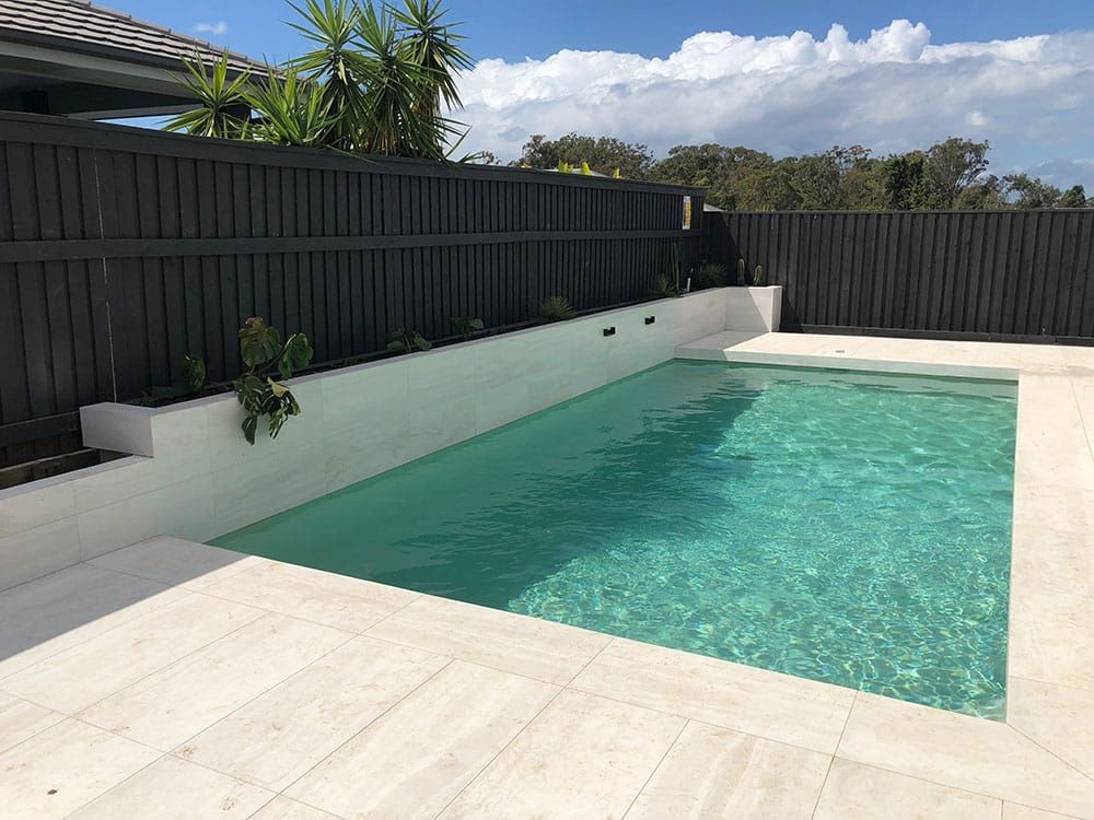 A Large Swimming Pool With a Black Fence Surrounding It — Pools By Design in Warana, QLD