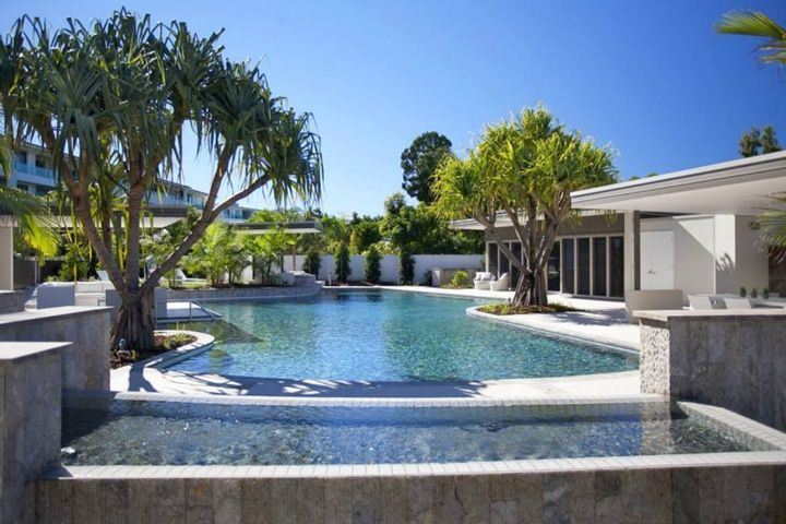 A Large Swimming Pool Surrounded by Palm Trees and a Building — Pools By Design in Warana, QLD