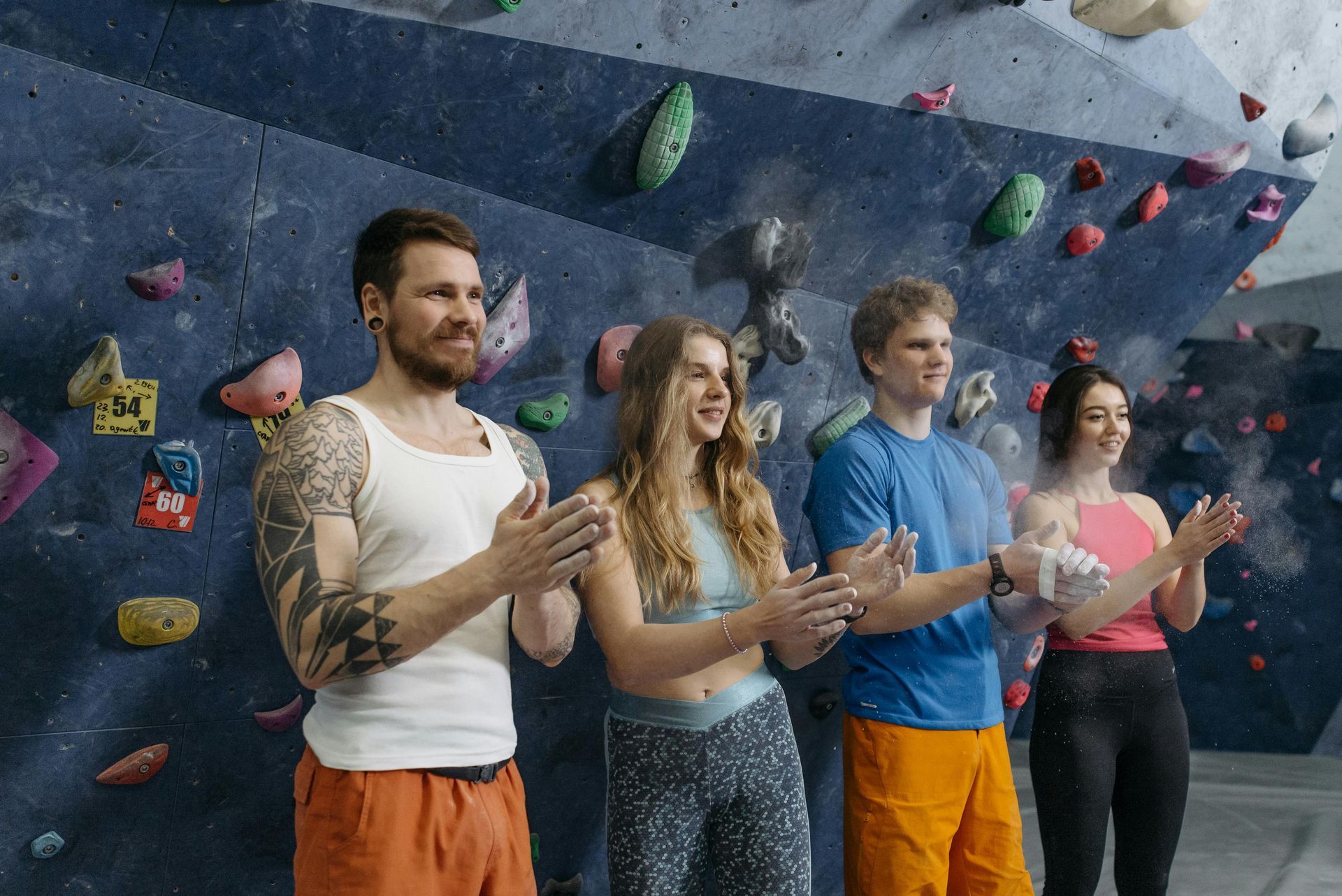 Four people clapping in front of a climbing wall. They appear happy.