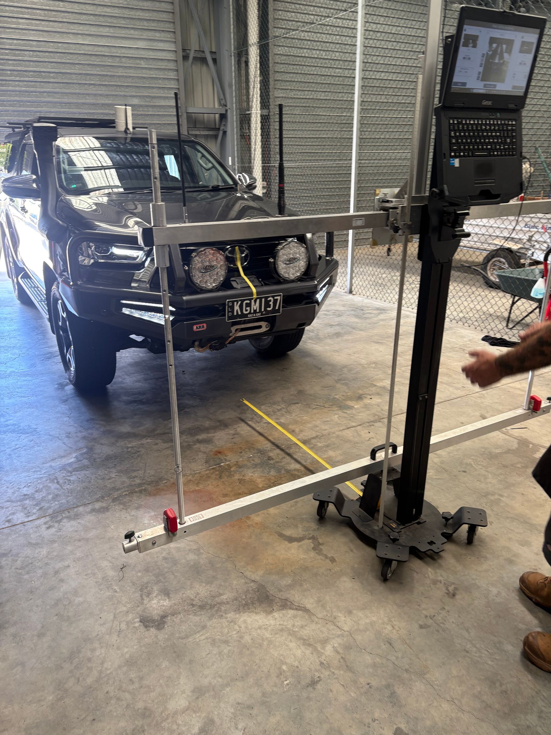 A dark pickup truck undergoing alignment check in a garage. A laptop displays data, and a technician is present.— Airlie Beach Smash Repairs in Cannonvale, QLD