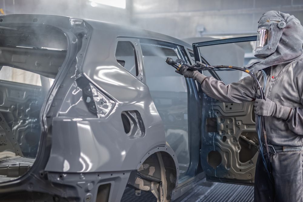 Worker in Protective Suit Sprays Paint on a Car Frame in a Factory Setting — Airlie Beach Smash Repairs in Bowen, QLD