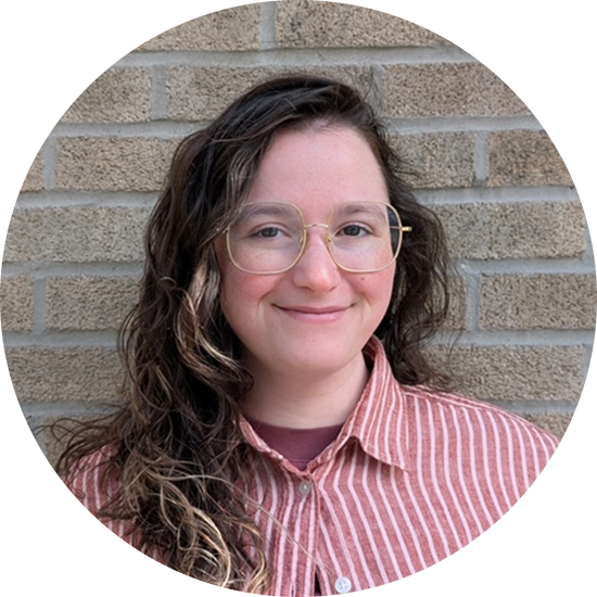 Woman with long brown hair smiles at the camera, wearing a cream sweater against a green background.