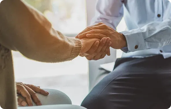 A person in a blue shirt holds hands with another person, offering comfort and support, indoors.