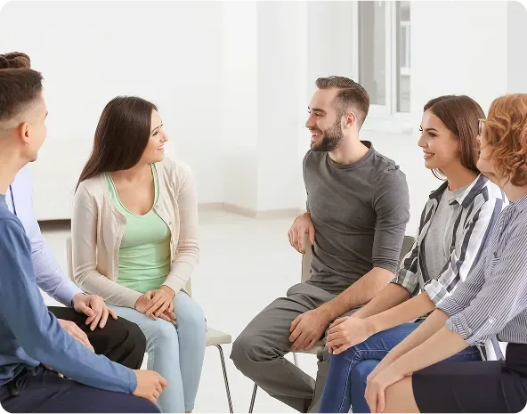 Group therapy session: Five people seated in a circle, smiling and talking in a brightly lit room.
