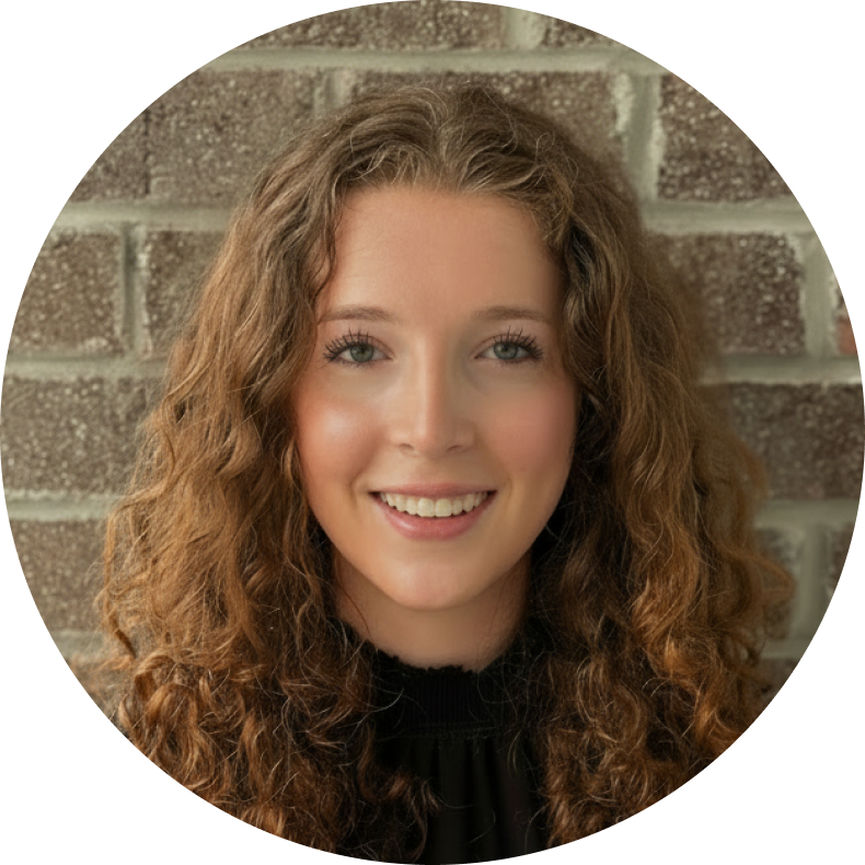 Woman in orange graduation sash smiles outdoors in front of a building.