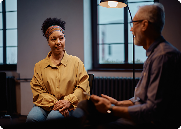 Group therapy session: Five people seated in a circle, smiling and talking in a brightly lit room.