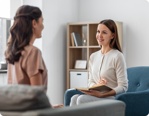 Young woman with dark hair smiling, talking on a cell phone at a desk. A plant and pens are in the background.