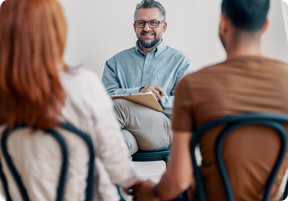 Young woman with dark hair smiling, talking on a cell phone at a desk. A plant and pens are in the background.