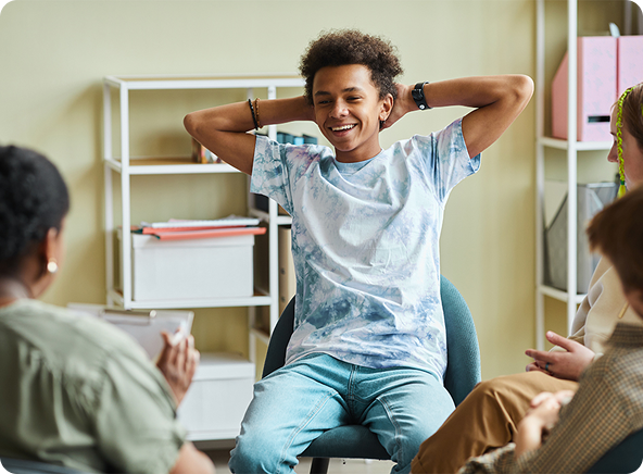 Teen boy smiling with hands behind head in a circle, in a counseling session.