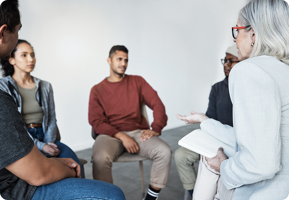 A group therapy session with a therapist and four diverse individuals seated in a circle, engaged in conversation.