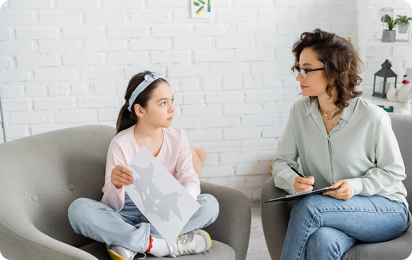 A woman gestures while speaking to a boy; both are seated on a couch, with the boy appearing sad.