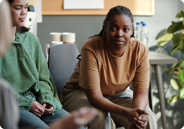Woman in a group therapy session; she sits forward with a concerned expression, looking at the person speaking.