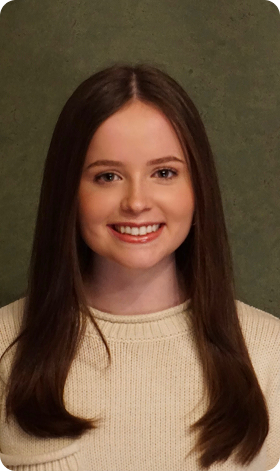 Woman with brown hair smiling, wearing a cream sweater. Green background.