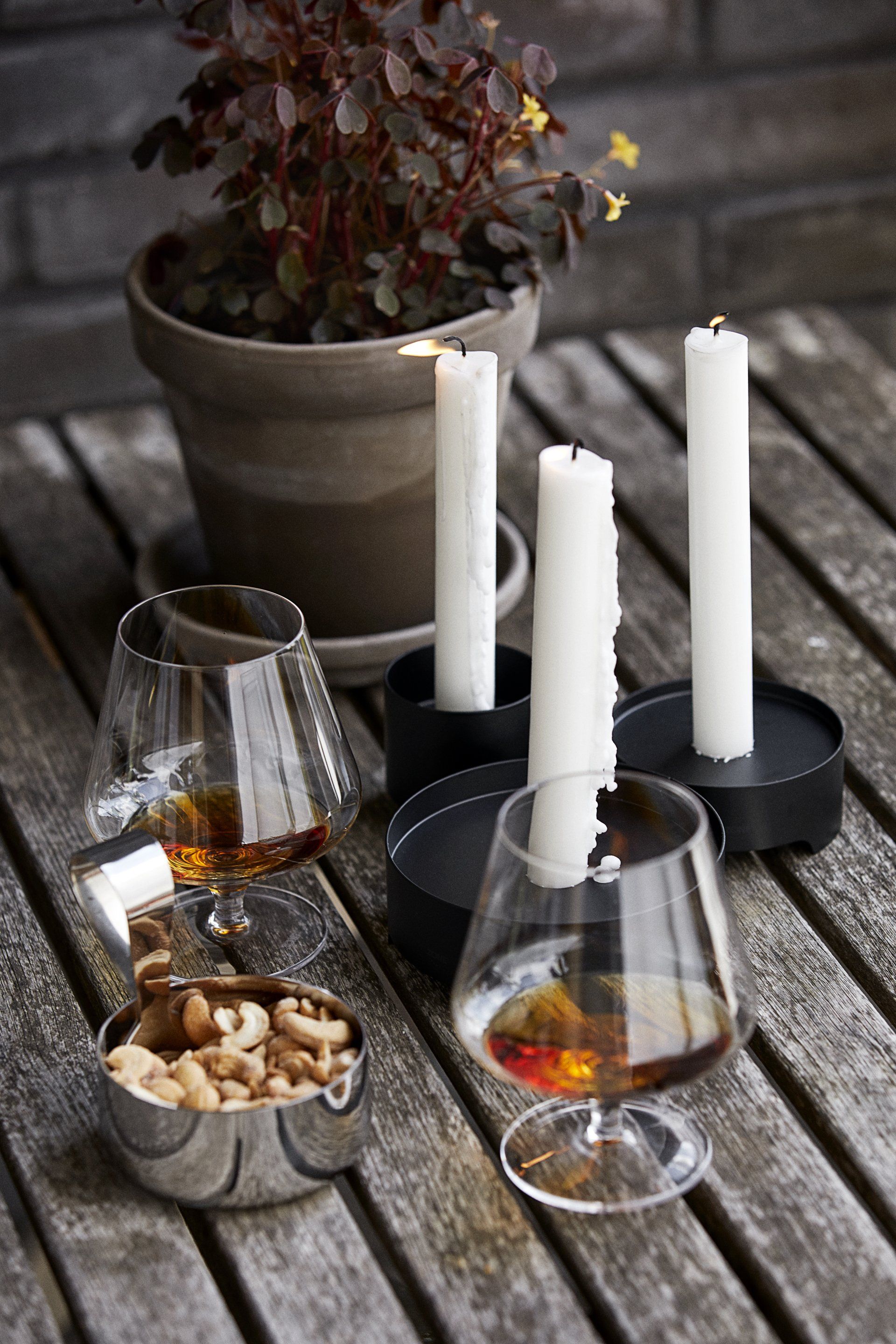 Ein Holztisch mit Kerzen, Weingläsern, Nüssen und einer Topfpflanze.