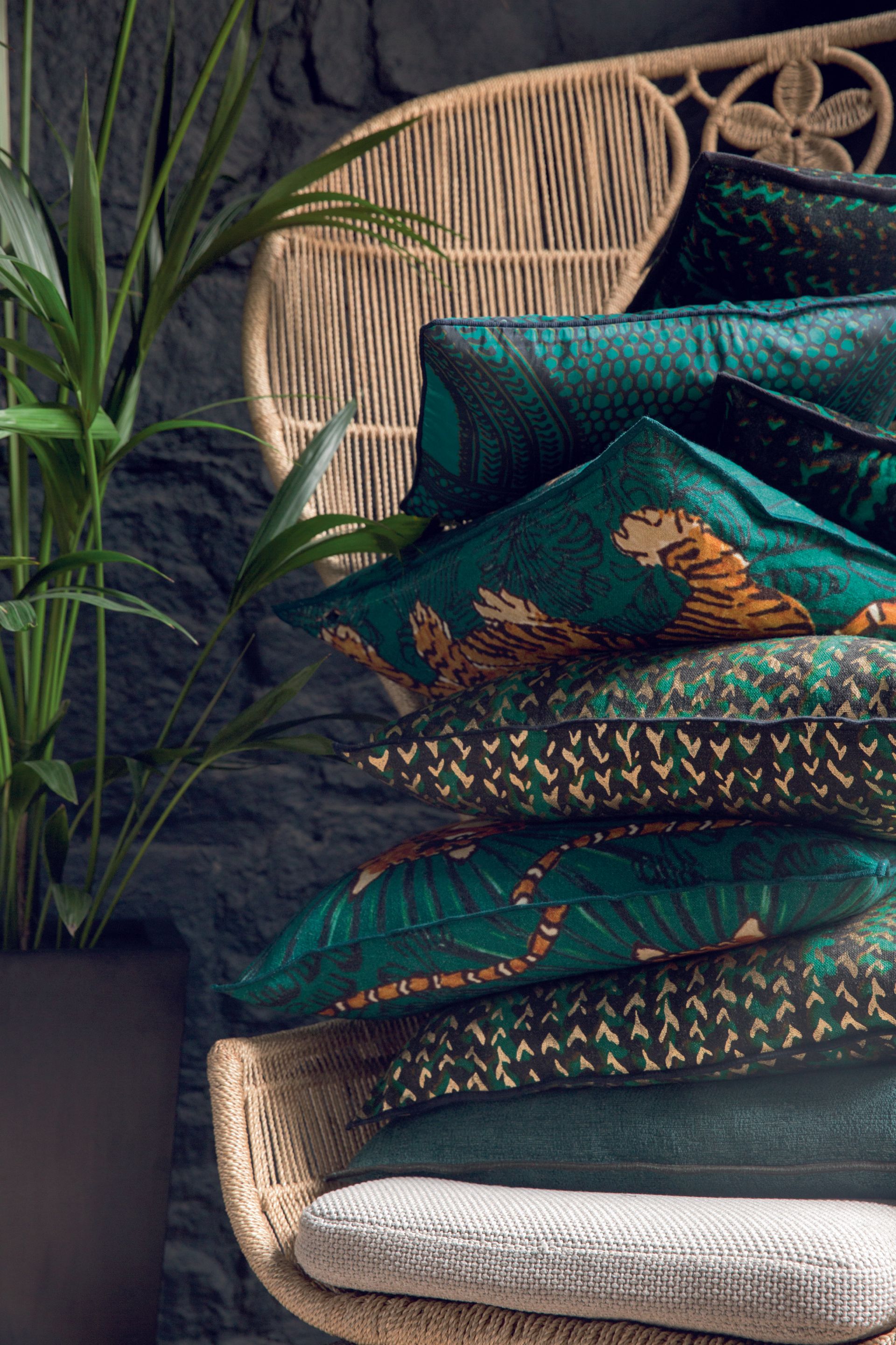 Ein Stapel grüner Kissen liegt auf einem Stuhl neben einer Pflanze.