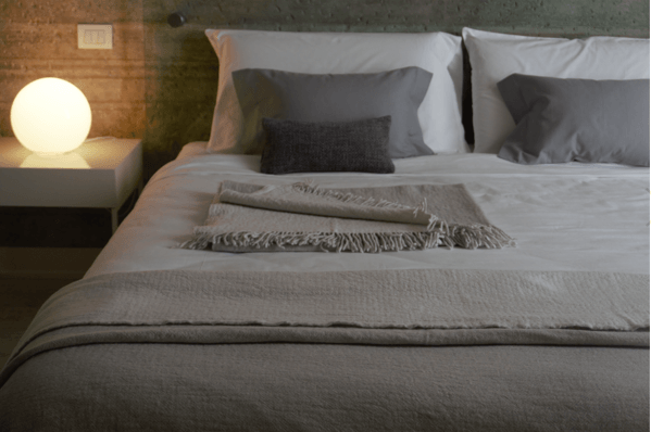 Ein Bett mit weißen Laken und grauen Kissen in einem Schlafzimmer