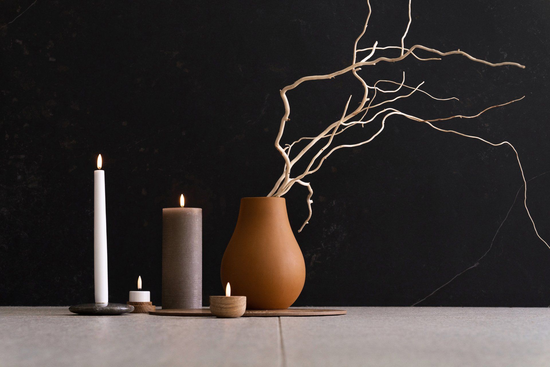Eine Vase mit einem Zweig darin und Kerzen auf einem Tisch.