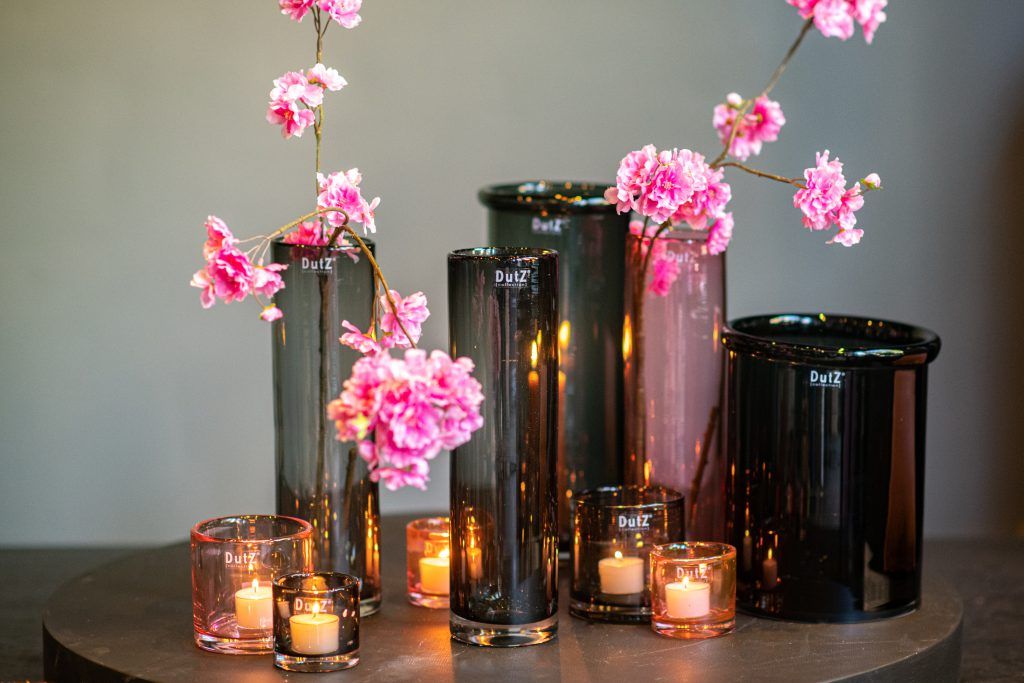 Eine Gruppe von Vasen gefüllt mit rosa Blumen und Kerzen auf einem Tisch.