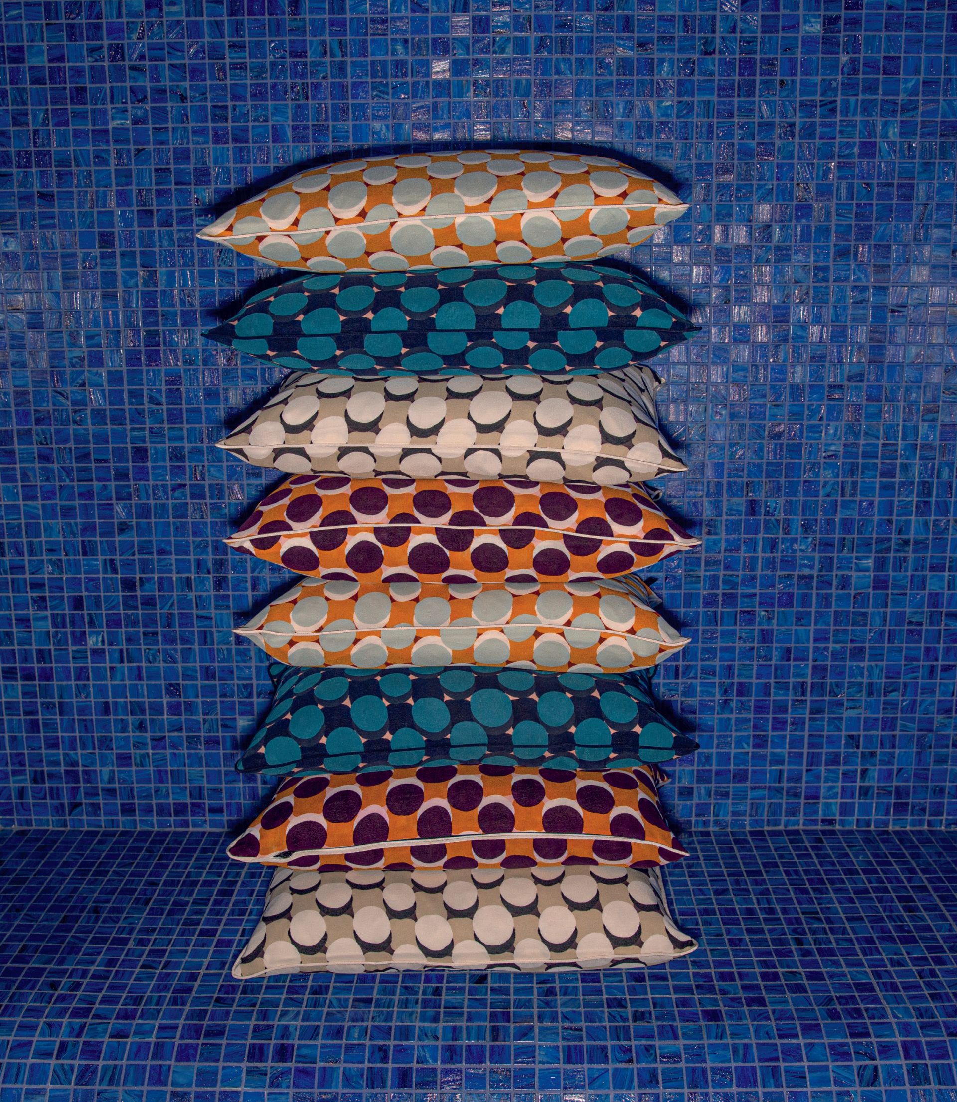 Ein Stapel bunter Kissen vor einer blau gefliesten Wand.