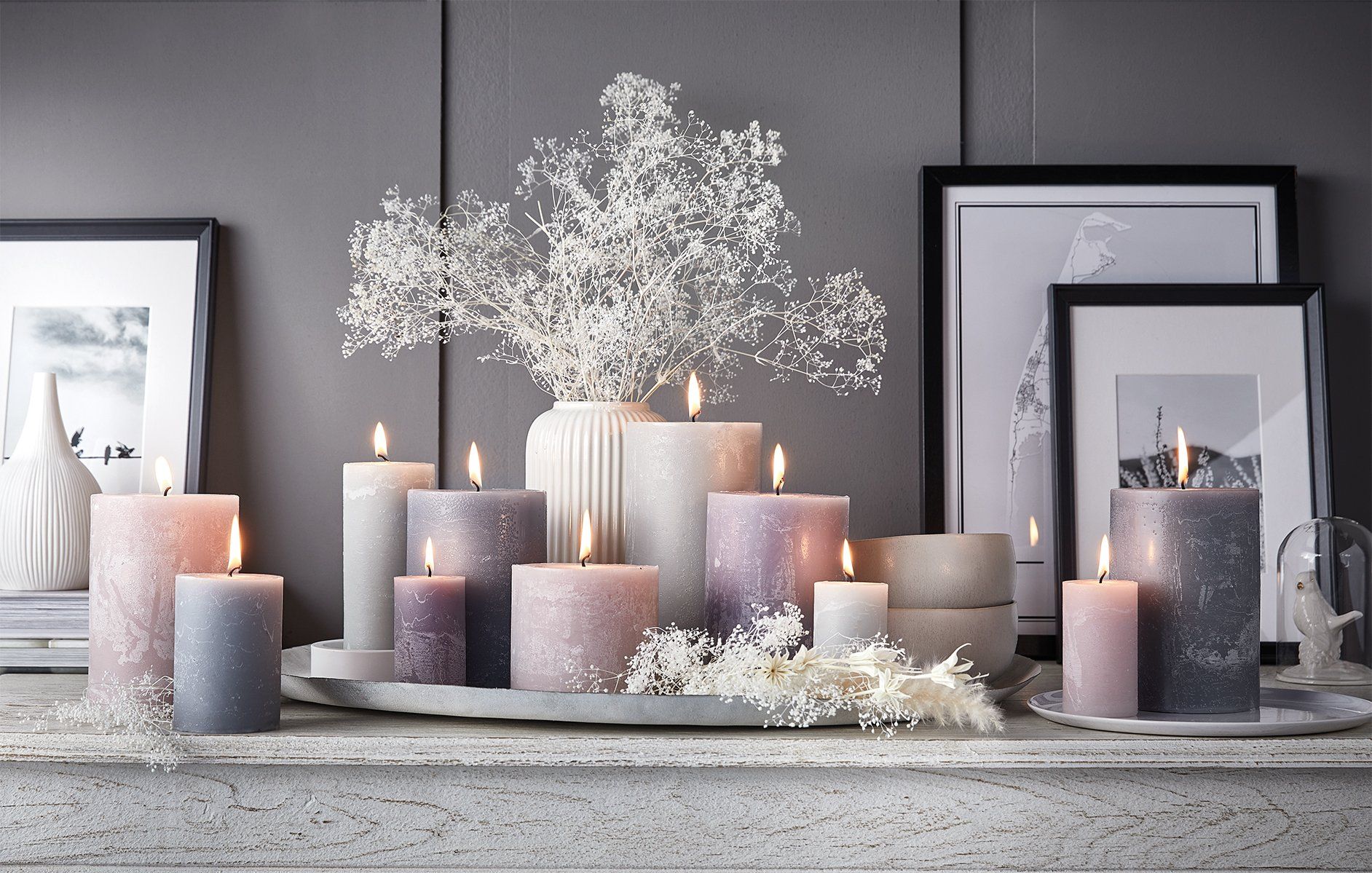 Ein Bündel Kerzen steht auf einem Kaminsims neben einer Vase mit Schleierkraut.