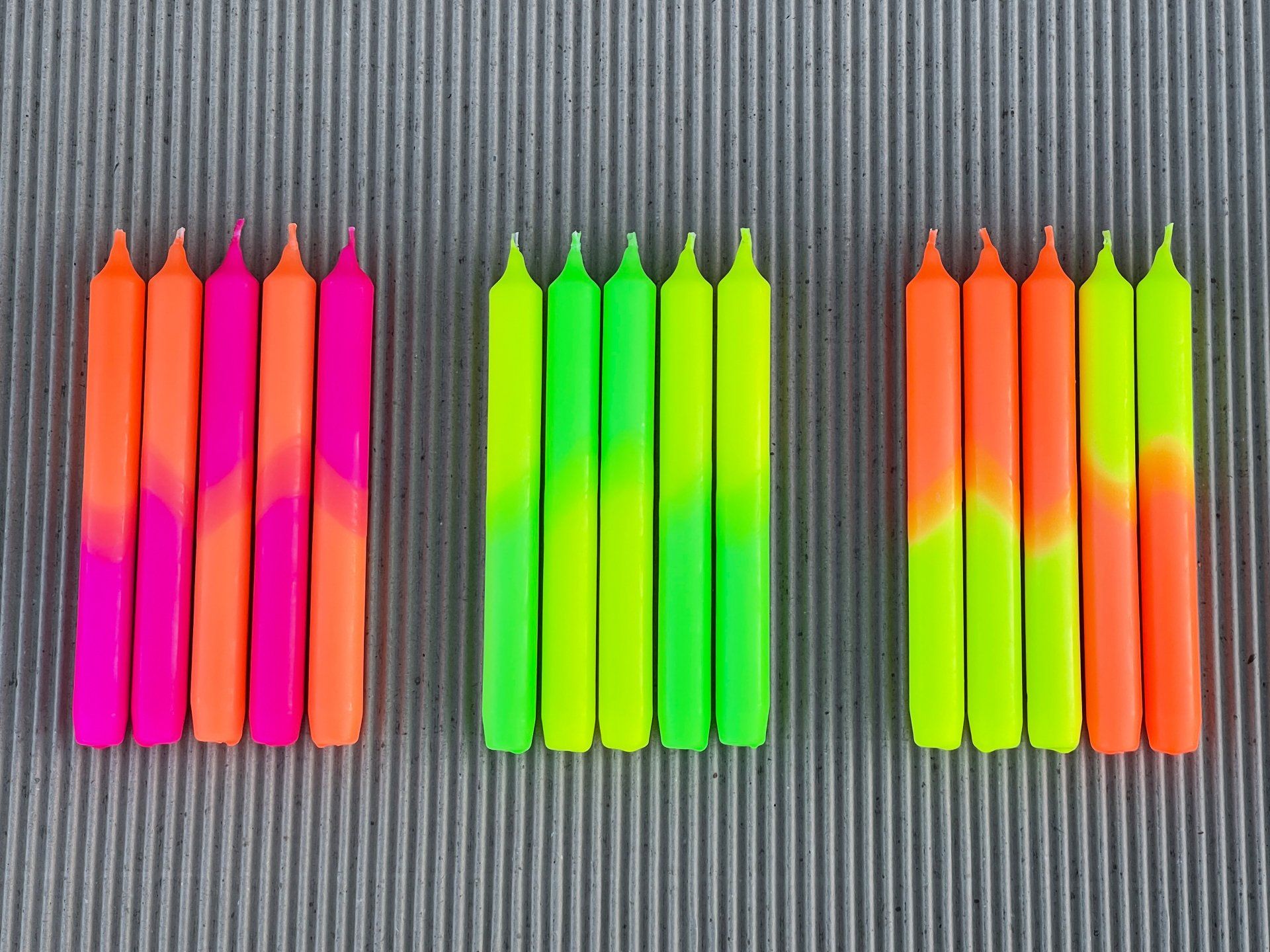 Eine Reihe neonfarbener Kerzen steht auf einer Pappoberfläche.
