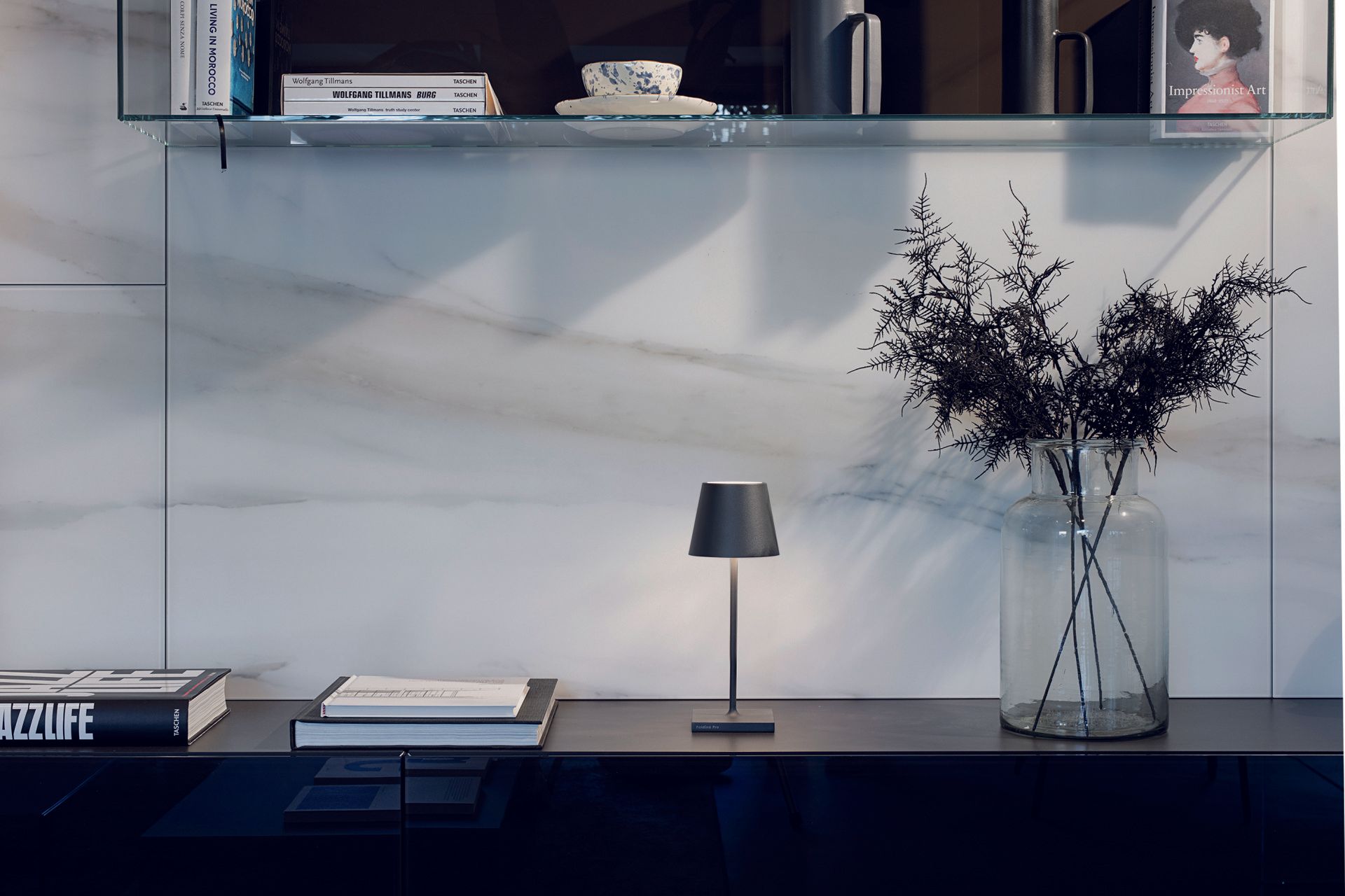 Eine Vase mit Blumen steht auf einem Regal neben einer Lampe.