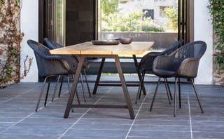Ein Tisch und Stühle stehen auf einer Terrasse neben einem Fenster.