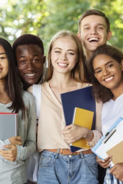 Group of smiling students with books outdoors.