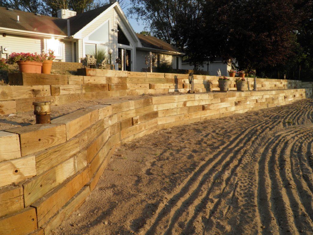 Wooden retaining wall curving towards a house, with sand and potted plants. Wooden retaining wall curving towards a house, with sand and potted plants.