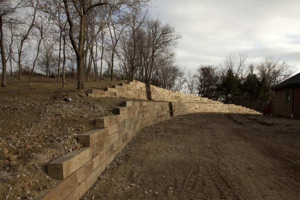 Retaining wall made of blocks with hillside behind it. Dry, brown landscape with trees, cloudy sky. Retaining wall made of blocks with hillside behind it. Dry, brown landscape with trees, cloudy sky.