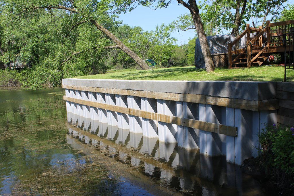 Concrete and wood retaining wall along a body of water with trees in the background. Concrete and wood retaining wall along a body of water with trees in the background.