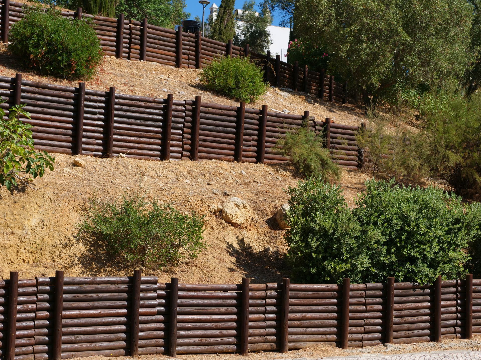 Brown log retaining walls on a hillside with green bushes and trees. Brown log retaining walls on a hillside with green bushes and trees.
