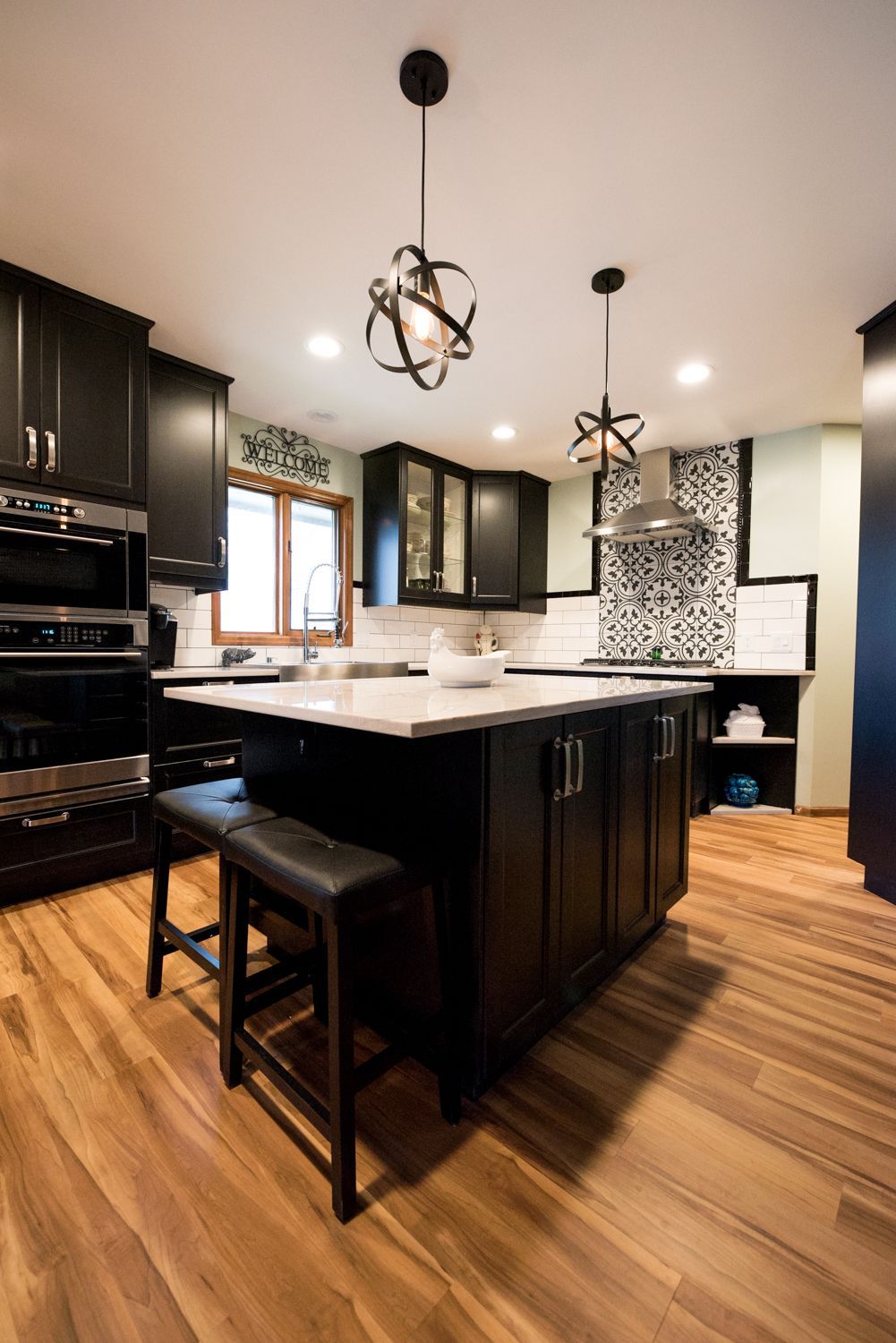 Modern kitchen with white cabinets, blue island, gold accents, stainless steel appliances, and decorative lighting.