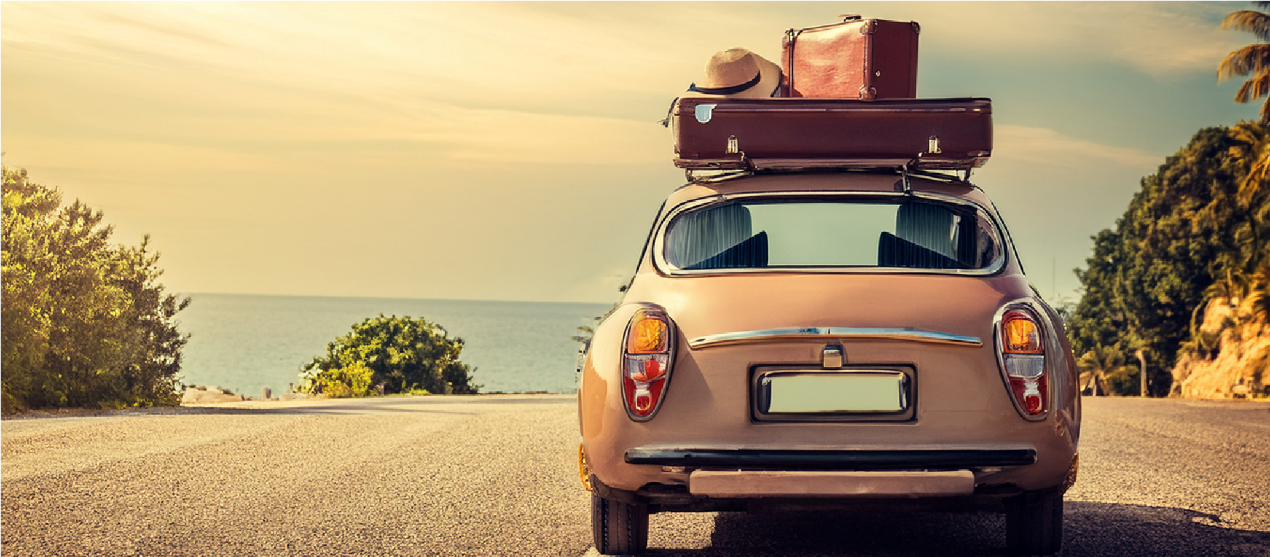Vintage car with luggage on roof, parked on a road by the sea at sunset