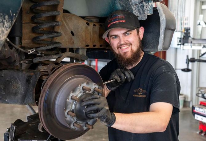 Mechanic smiling while working on a car brake assembly in a garage