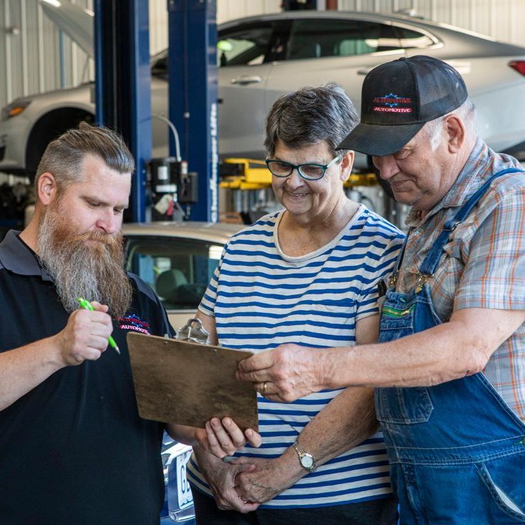 Three people in an auto shop review a clipboard near a car lift and vehicle.