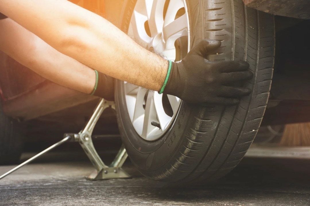 Gloved hands changing a car tire with a jack on the road