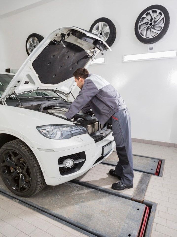 Mechanic inspecting a white car with its hood open in a garage at an inspection bay