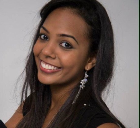 A woman wearing a black shirt and earrings smiles for the camera