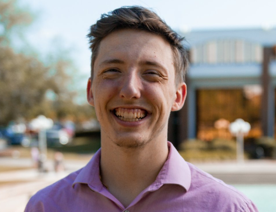 A young man in a purple shirt is smiling for the camera.