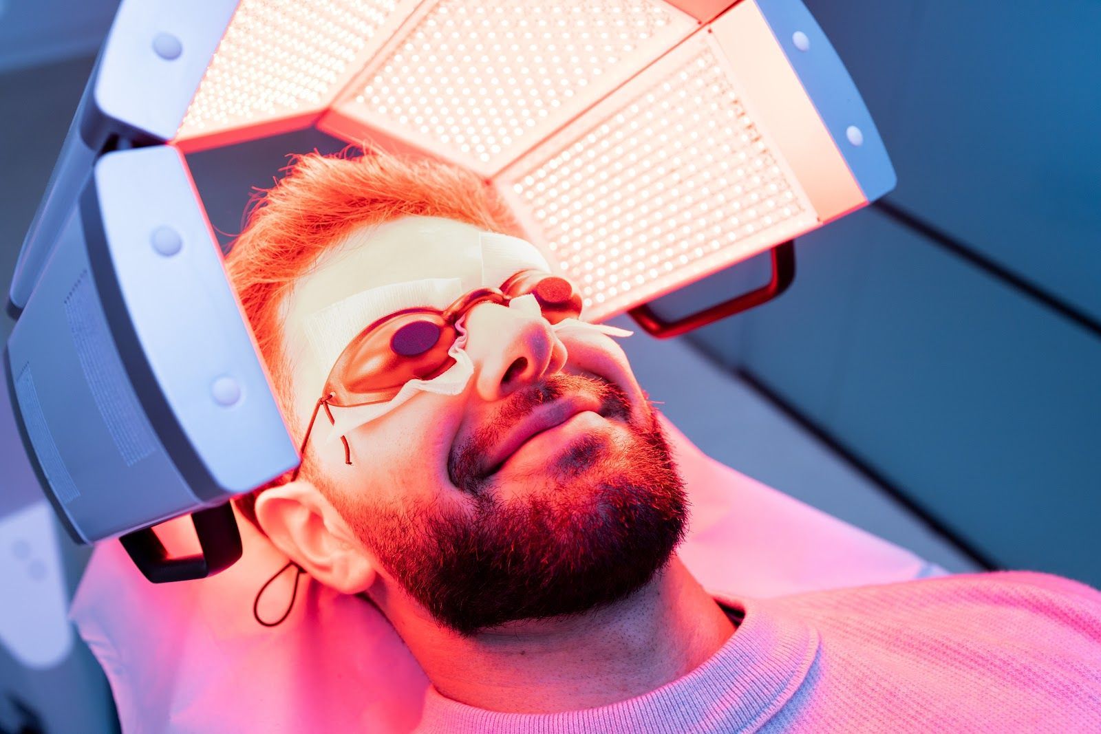 Person wearing protective glasses under bright red and blue lights in a clinical or lab setting