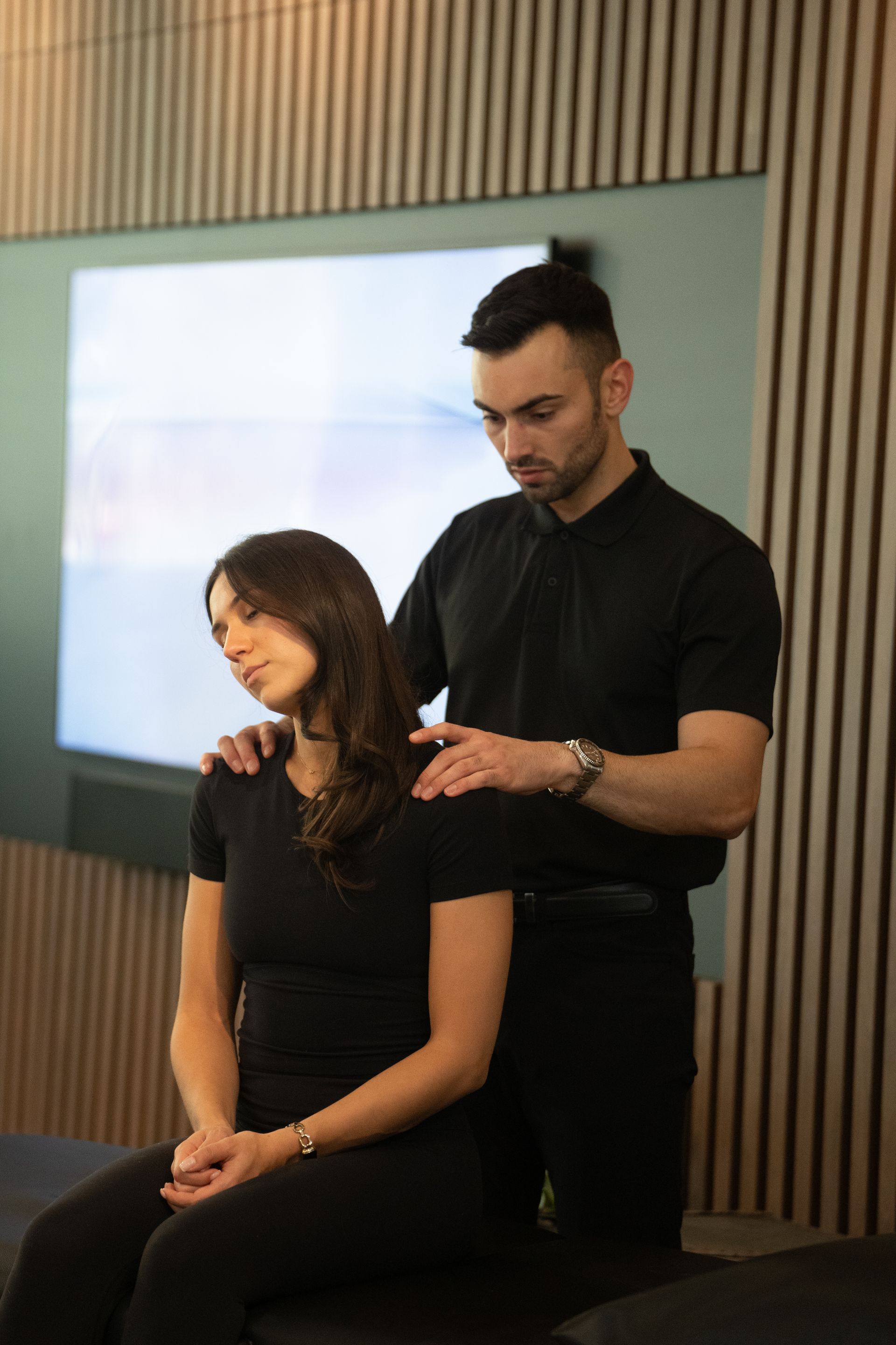 Hair stylist cutting a seated woman’s hair in a salon with a screen behind them