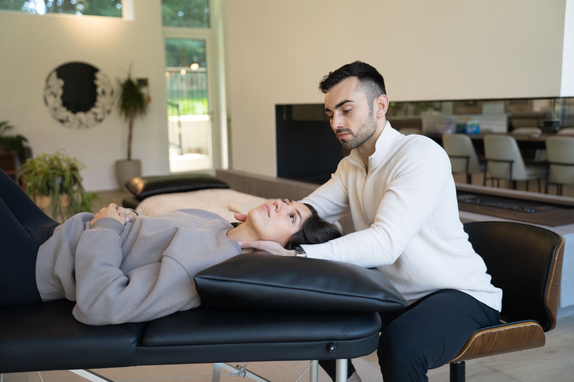Therapist leaning over a client lying on a treatment table in a bright clinic room