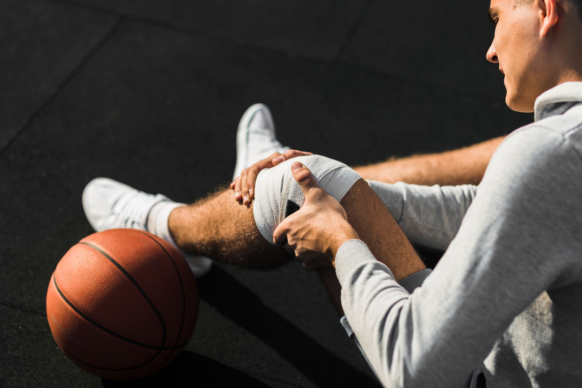 Injured basketball player sitting on the court holding his knee beside a basketball