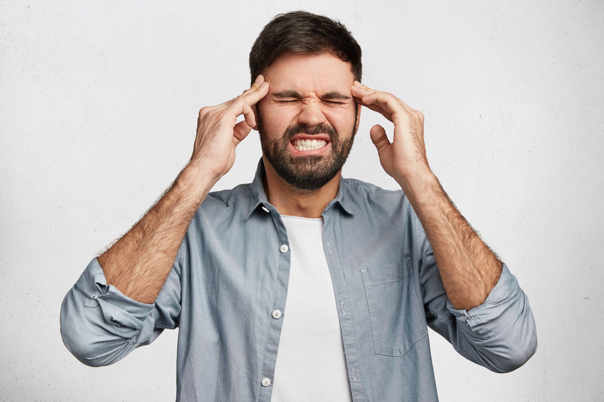 Man holding his temples with eyes shut, looking stressed against a plain white background