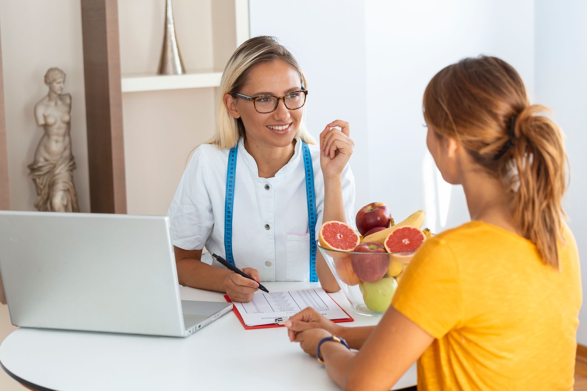 Doctor talking with a patient at a desk, with a laptop and fruit bowl in a bright office