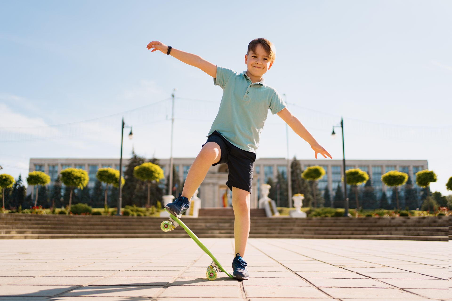 Boy balancing on a skateboard outdoors with arms outstretched in a sunny plaza