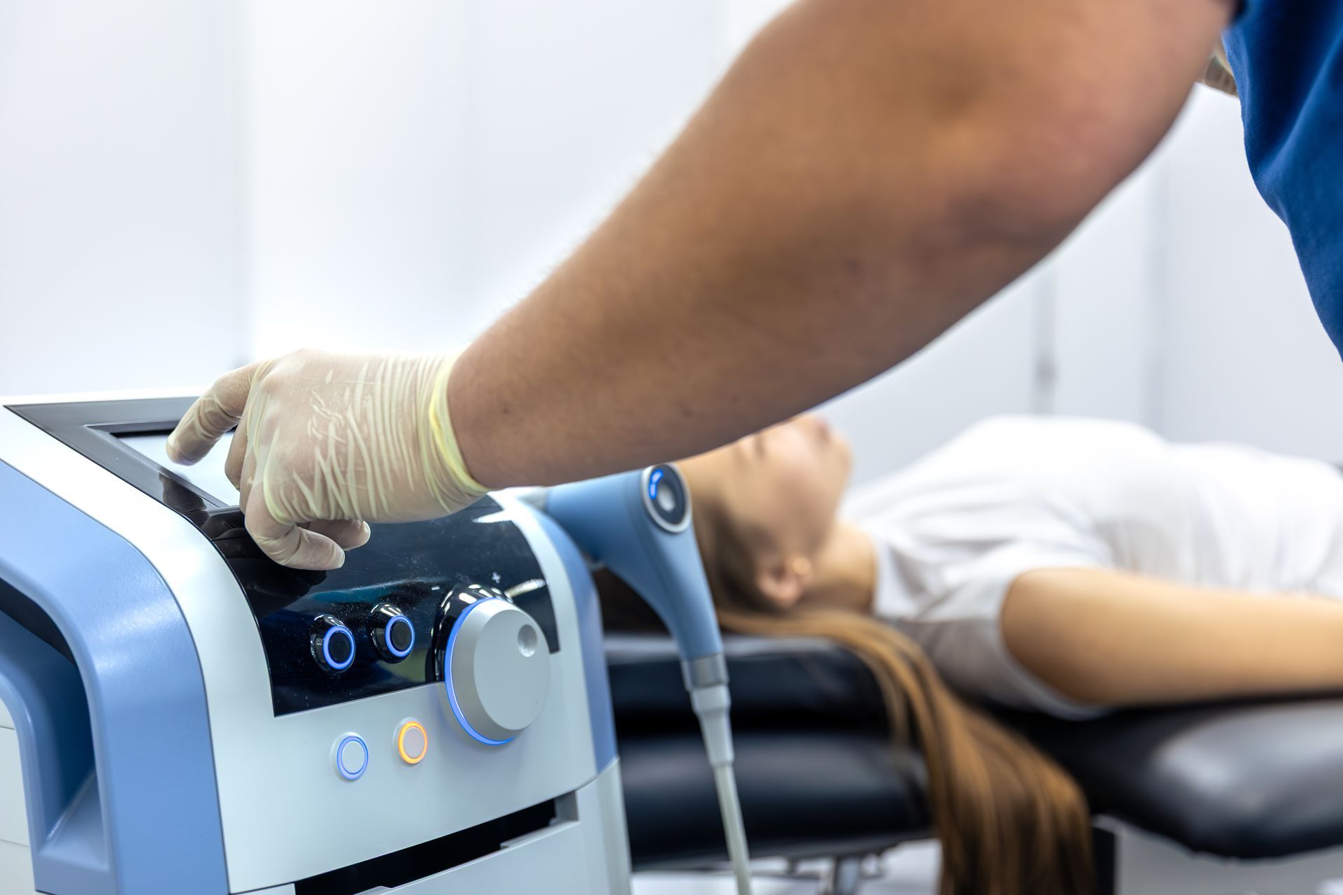 Gloved technician adjusting controls on a medical device beside a reclining patient in a clinic