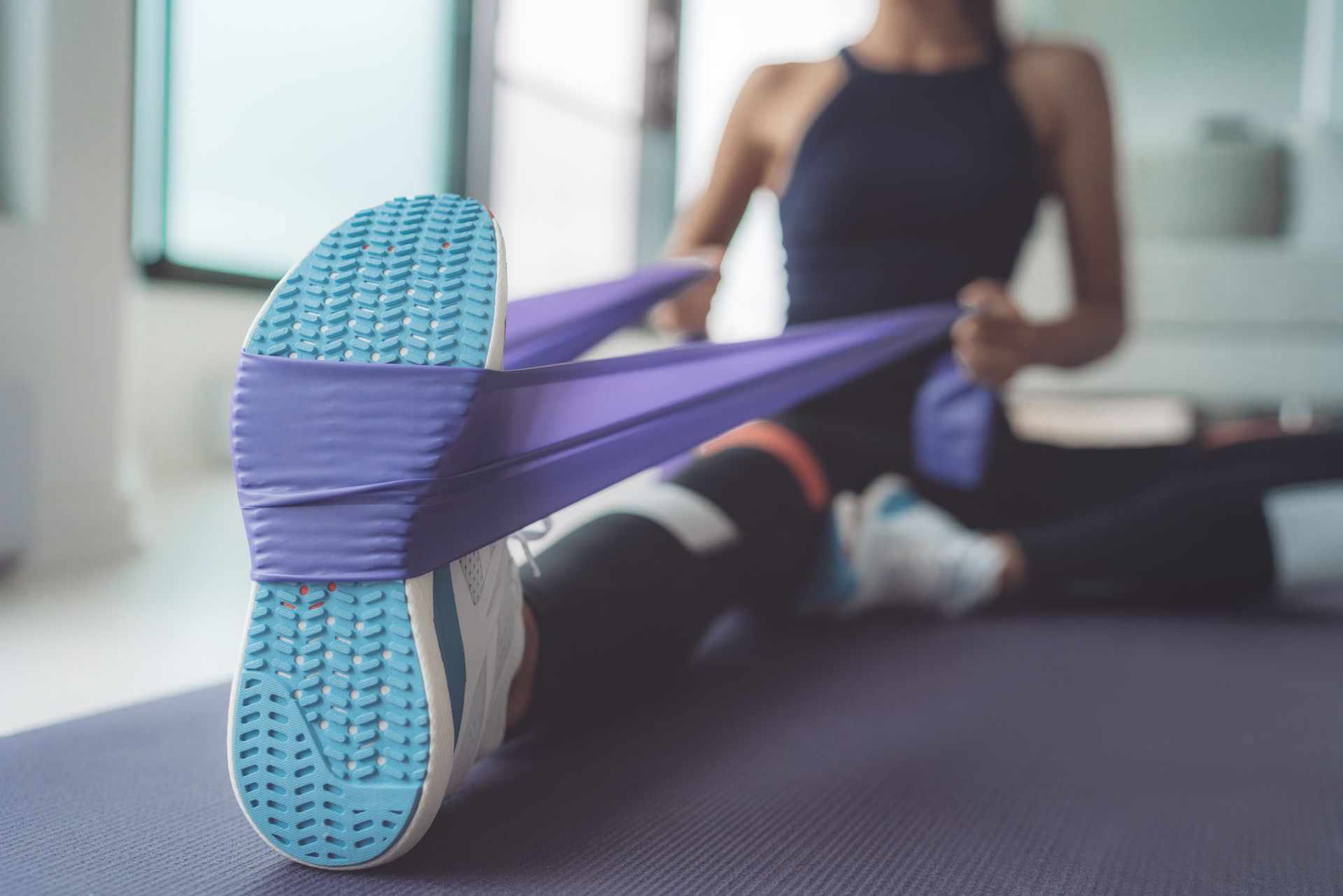 Person stretching with a purple resistance band in a gym, close-up of shoe sole in foreground